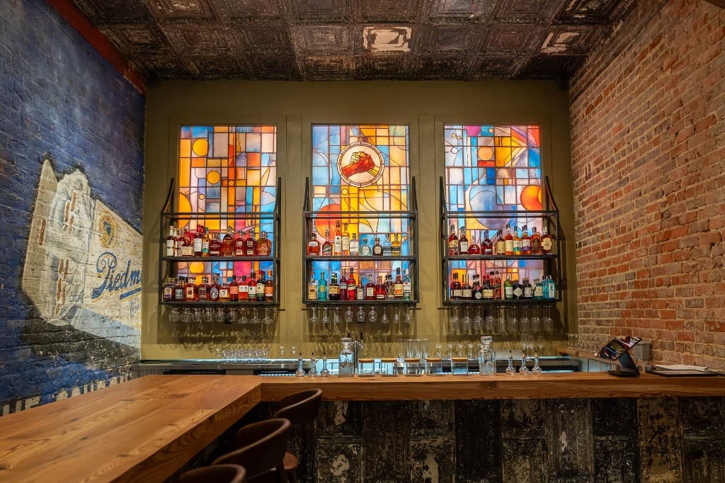 Speakeasy at Piedmont bar with stained-glass panels glowing behind shelves of bottles